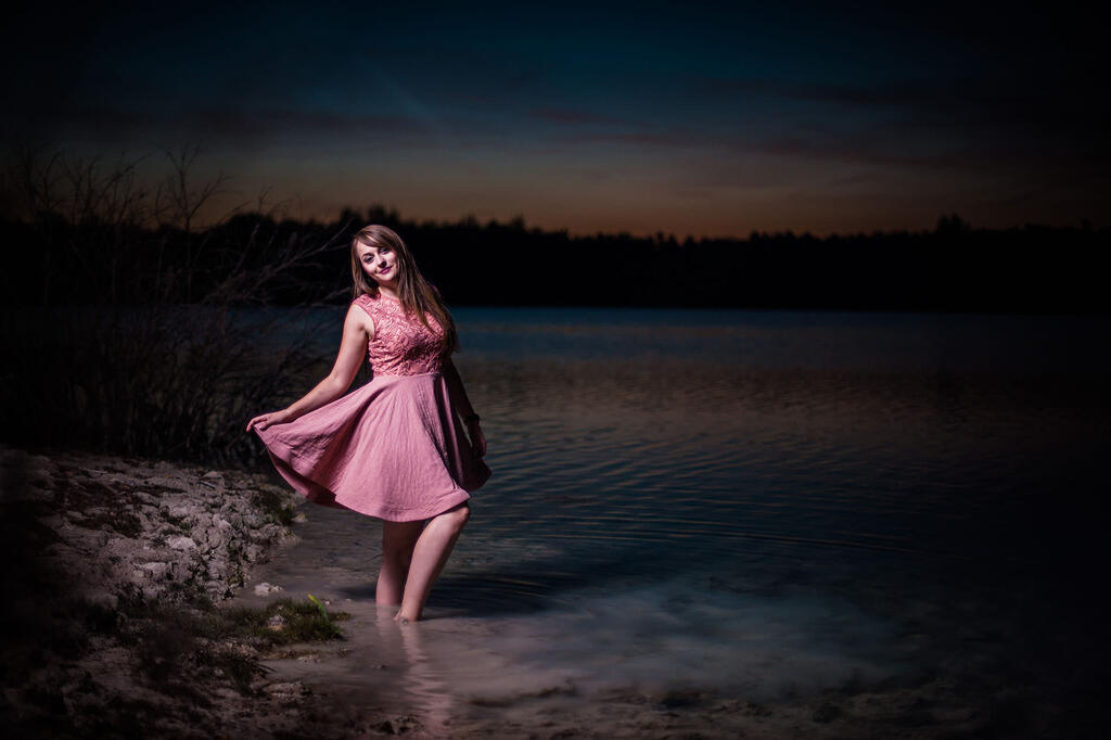 junge Frau in rosarotem Kleid nachts im See